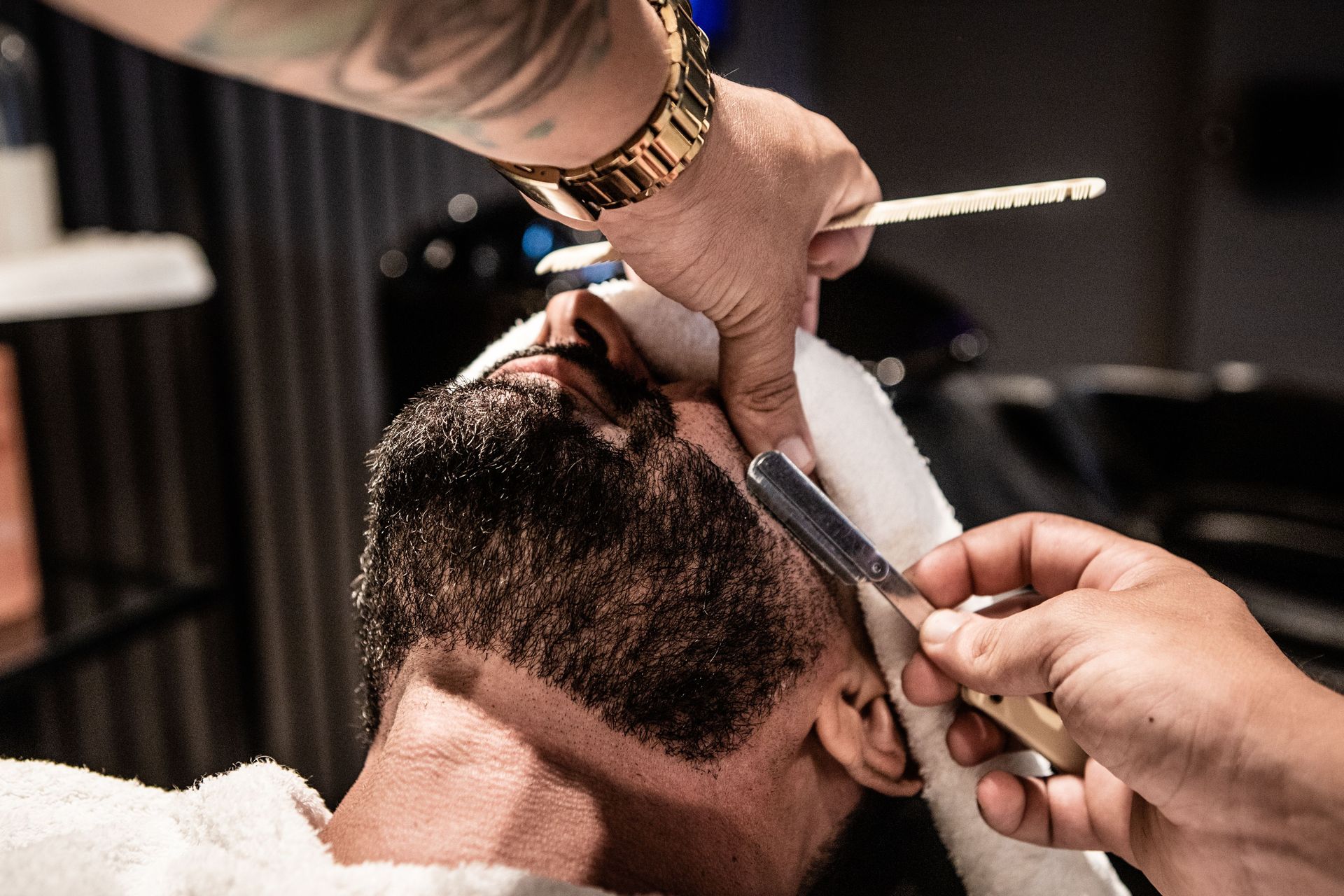A barber groomer trimming a beard with precise technique at a salon in João Pessoa, Brazil.