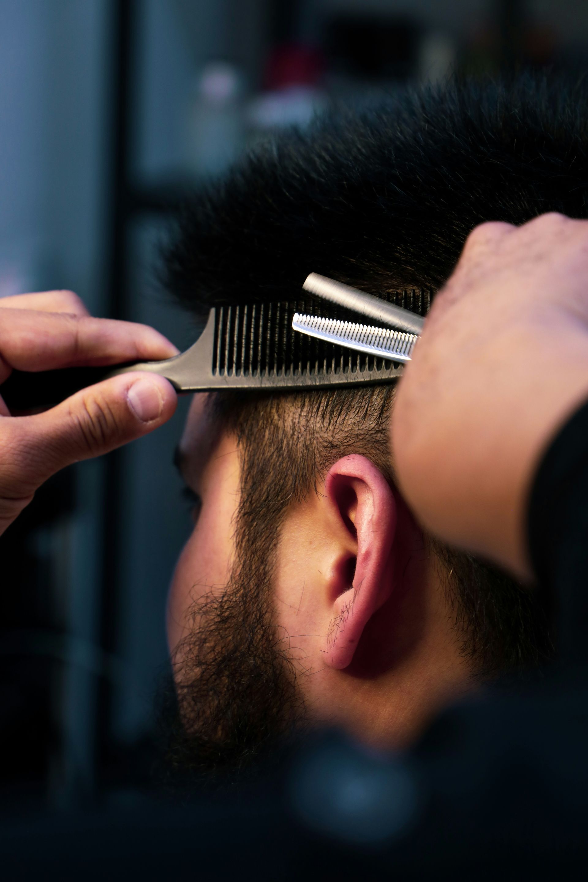 A barber using thinning shears and a comb to trim a man's hair