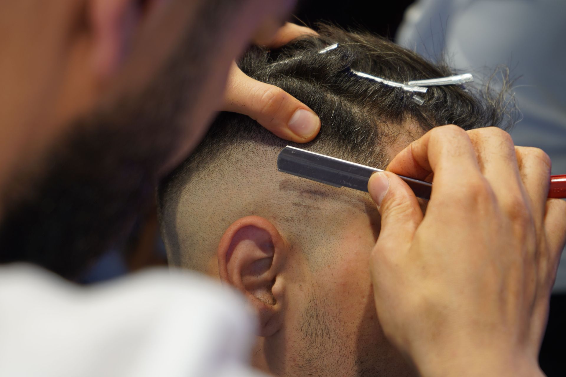 Close-up of a barber giving a modern haircut with a straight razor in a salon.