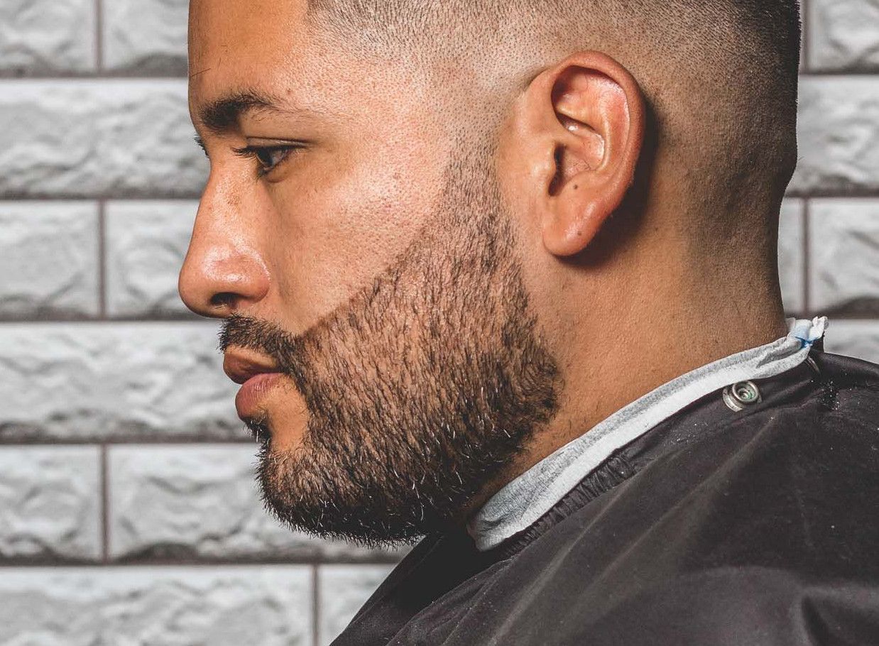 Side view of a man with a modern haircut and beard in a salon setting.