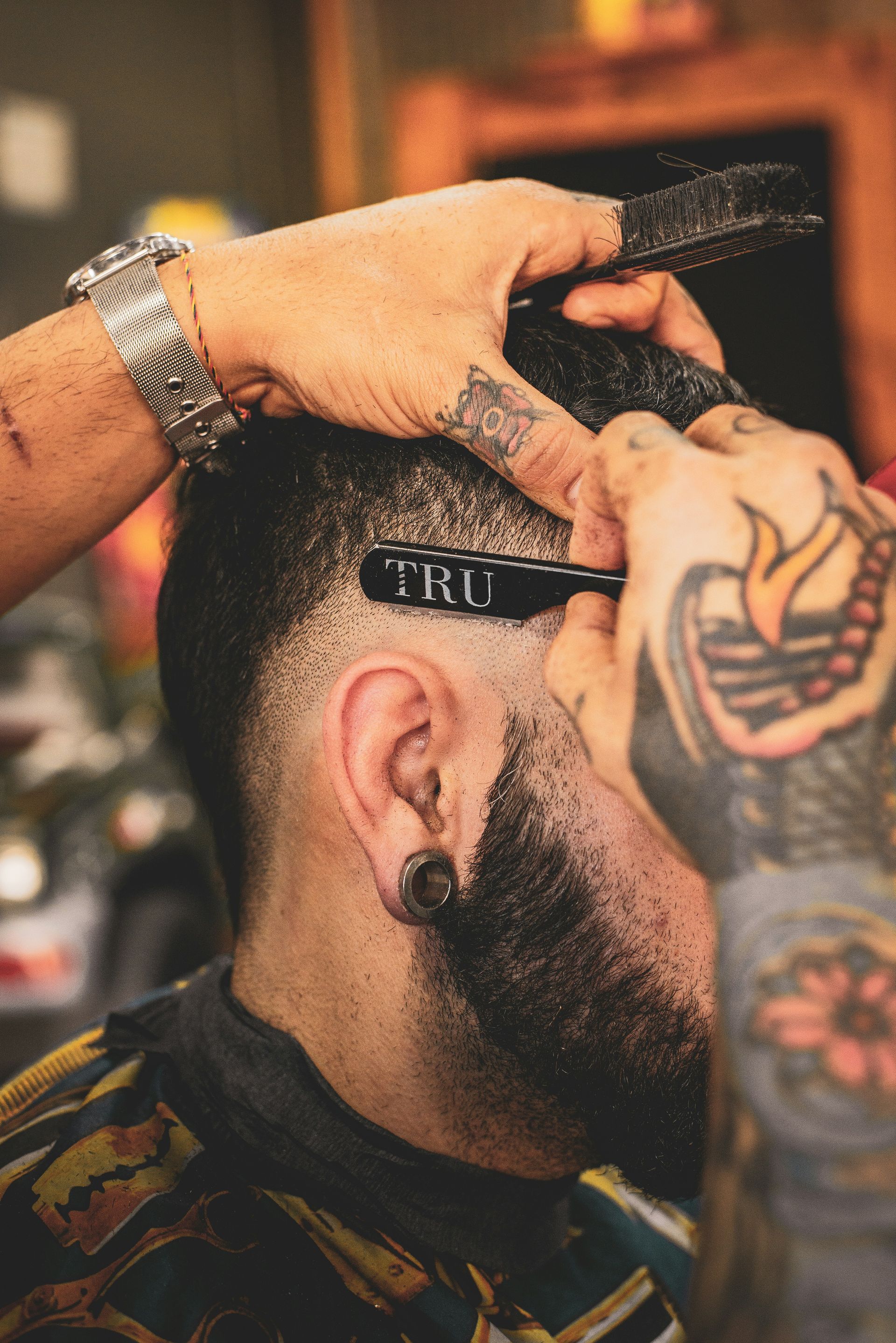A tattooed barber using a straight razor to trim a man's hair