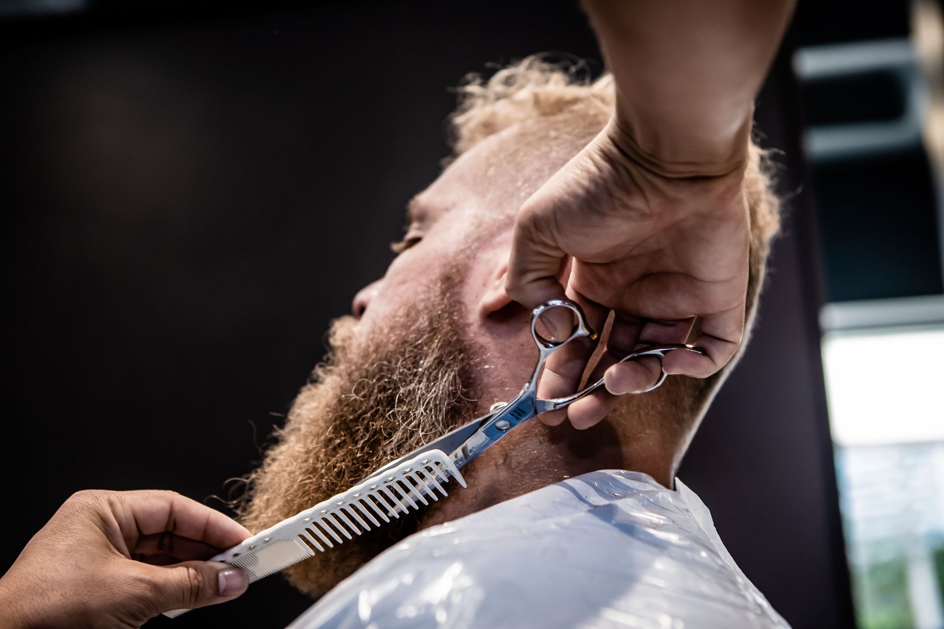 Close-up of a barber trimming a client's beard with scissors and comb.